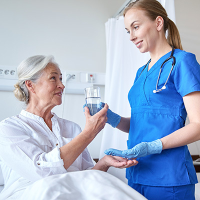 Nursing handing medication and a glass of water to a resident who is propped up in bed.